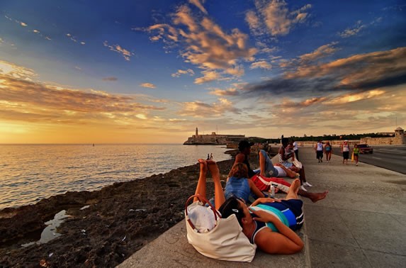 Personas viendo atardecer en el muro del Malecón