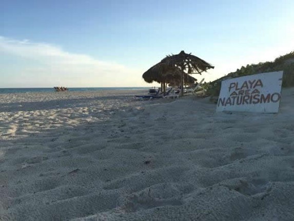 playa con sombrillas de guano y cartel en la arena