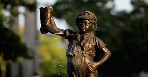 escultura de bronce de un niño sujetando una bota