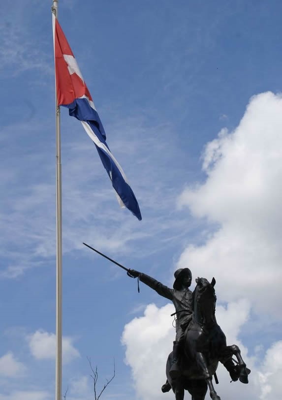 estatua de bronce y bandera cubana izada a su lado