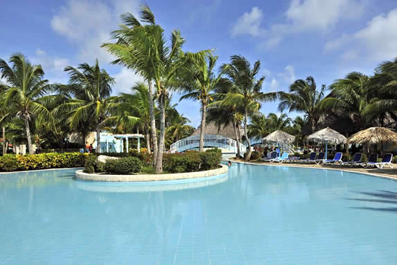 piscina rodeada de palmeras  y sombrillas de guano