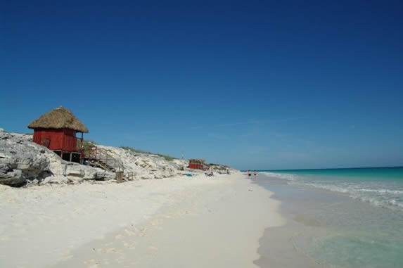 playa con rocas y casa de madera y techo de guano