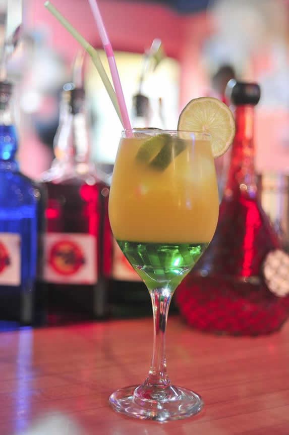 Glass with colorful drink and bottles in the back