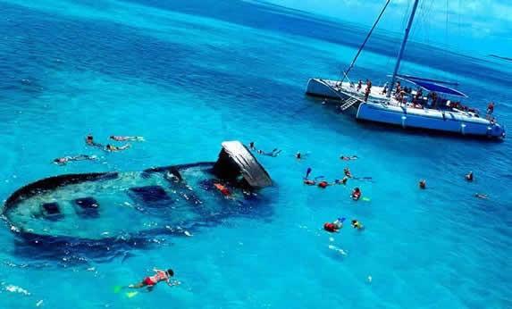 turistas haciendo snorkel alrededor de catamarán