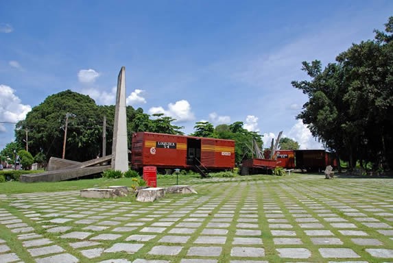 vagones rojos con escultura de piedra y árboles