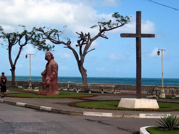 estatua de piedra con el mar al fondo y cruz